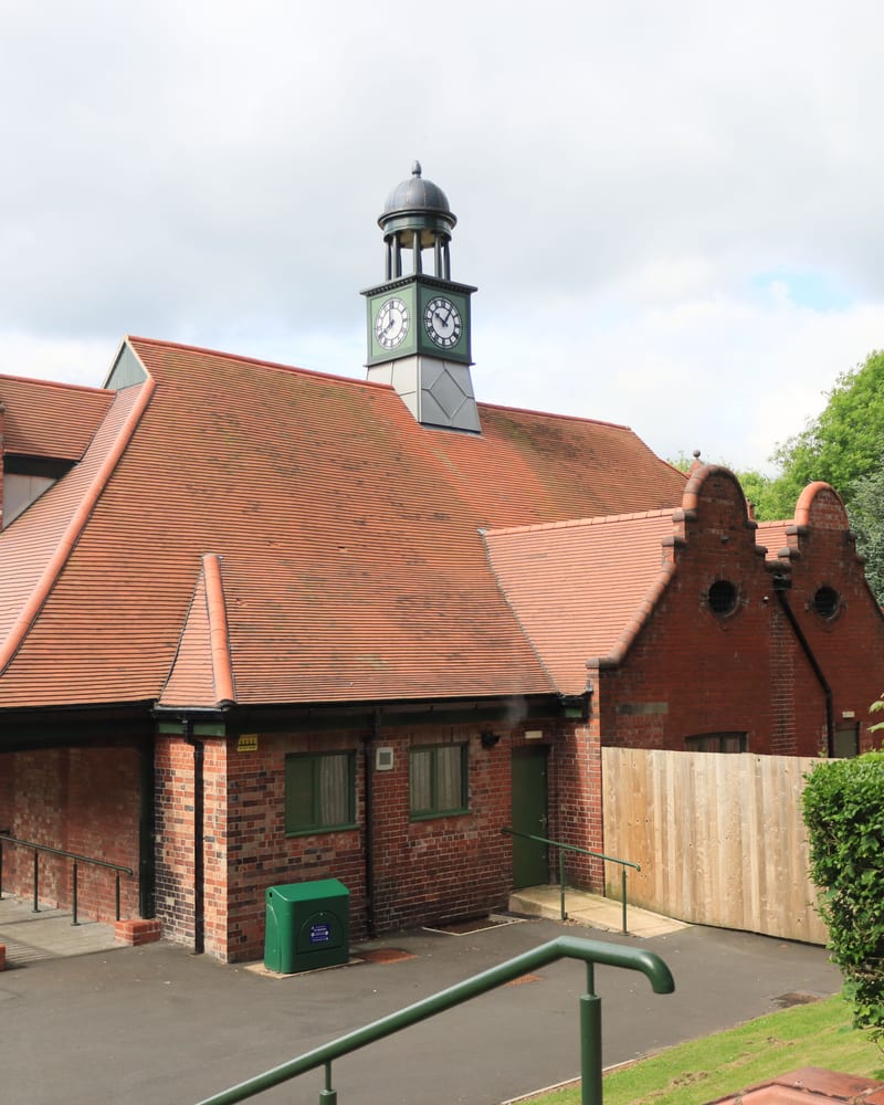 A red-brick building with a tiled roof and a clock tower, seen from an asphalt path.
